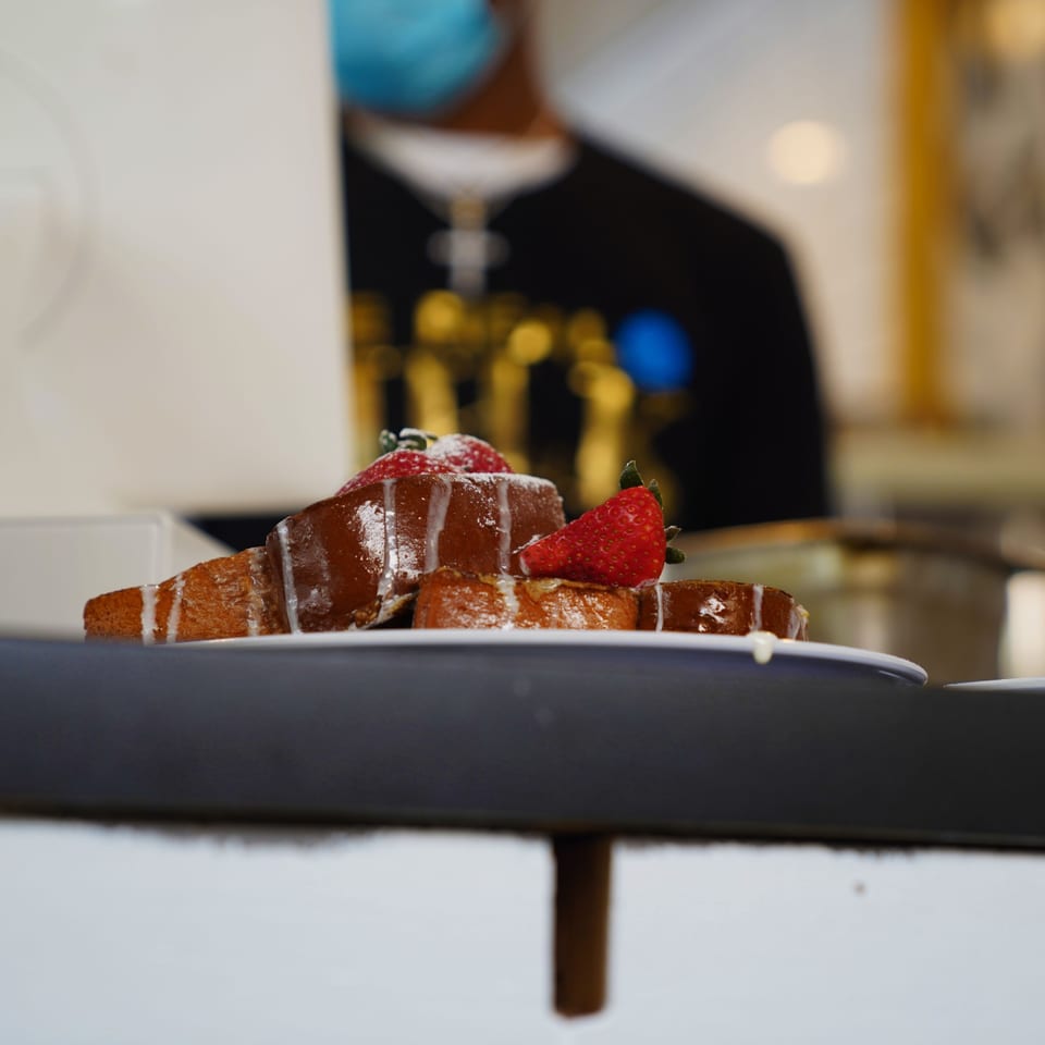 French toast with strawberries and powdered sugar, with a blurred person in the background.