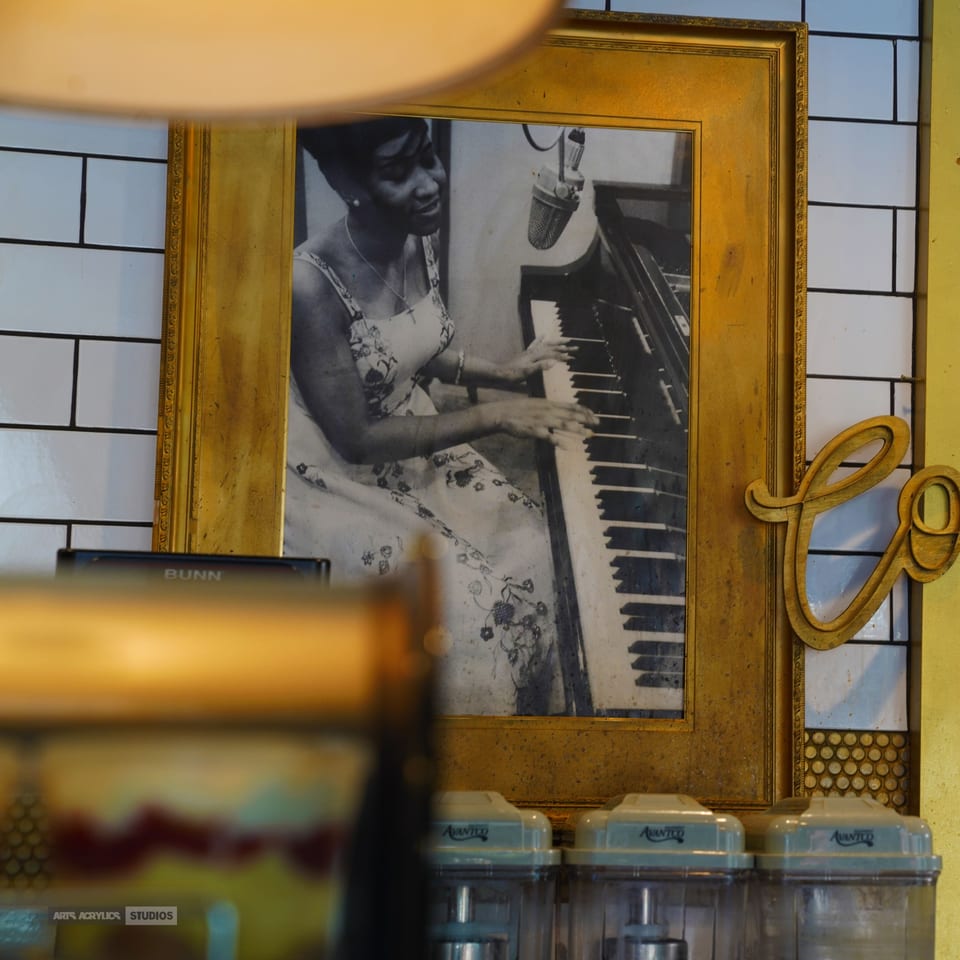 Black and white framed photo of a woman playing piano with a microphone, displayed at The Real Milk & Honey.