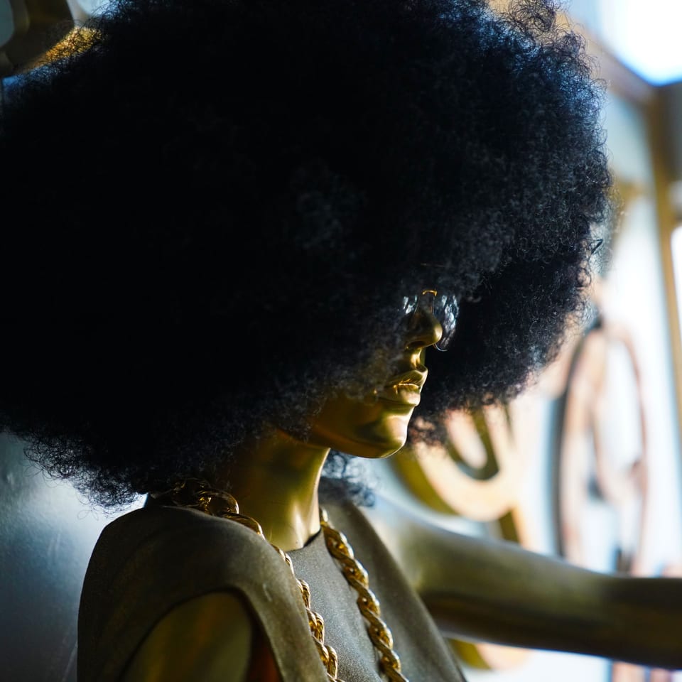 Golden mannequin with a large afro, sunglasses, and a gold chain, representing The Real Milk & Honey.