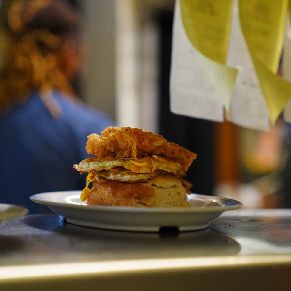 A stacked biscuit with fried chicken, two fried eggs, and gravy on a white plate.