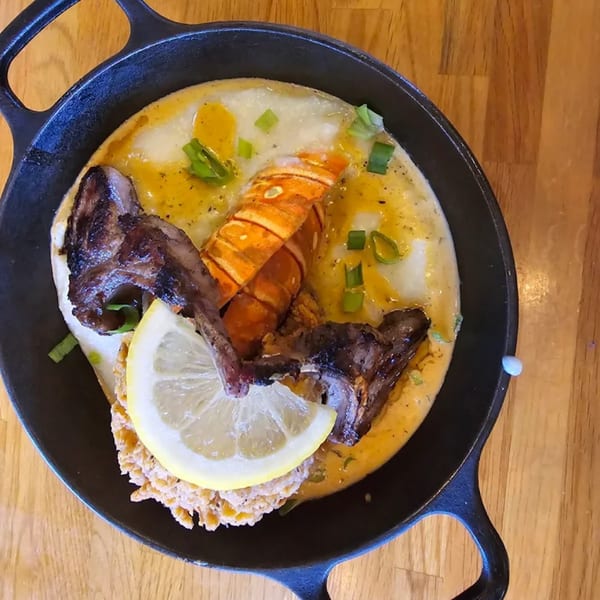 Lobster and grits with steak, a lemon slice, and green onions in a cast iron skillet.