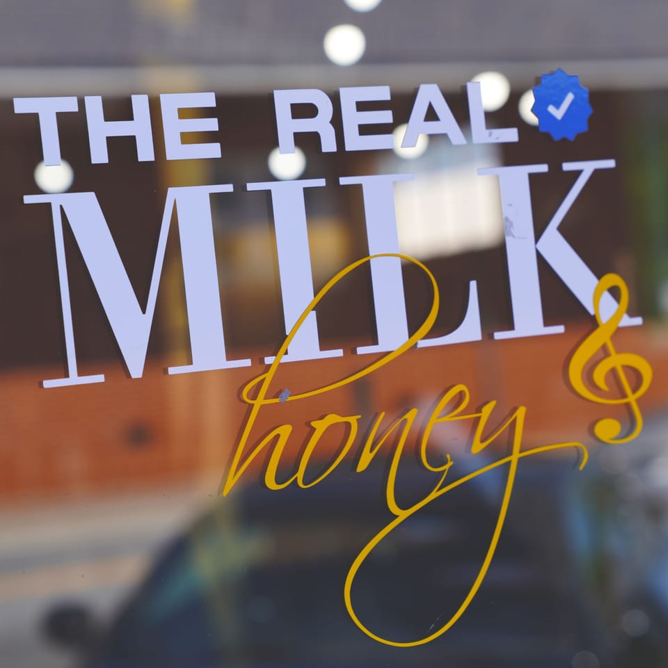 The Real Milk & Honey restaurant logo on a glass window with a blue verified checkmark.