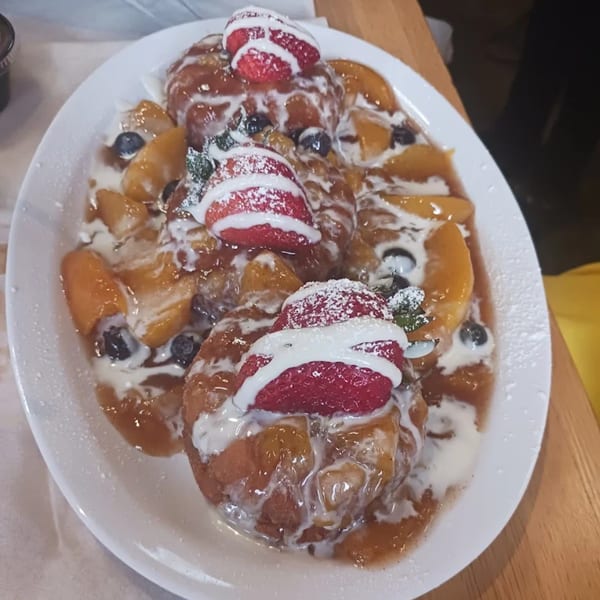 A plate of The Real Milk & Honey's French toast, topped with peaches, blueberries, strawberries, and cream.