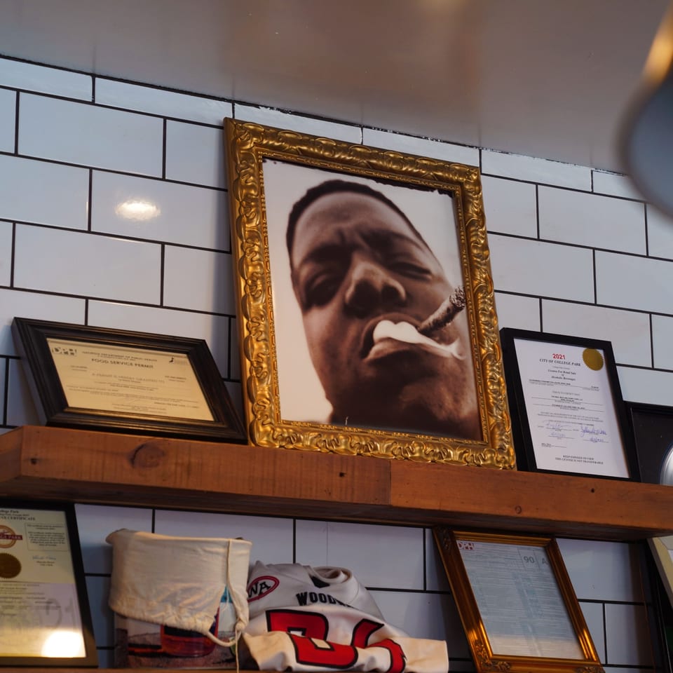 A framed portrait of Notorious B.I.G. smoking a cigar, with permits and a jersey on a shelf.