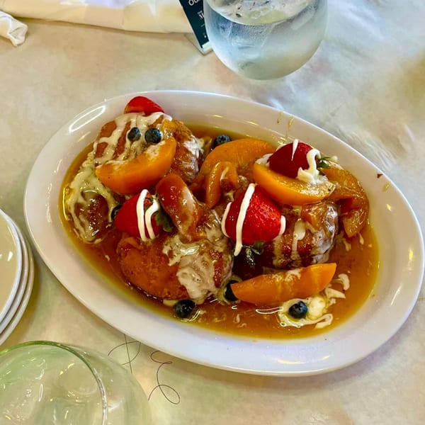 Golden French toast, peaches, strawberries, blueberries, and cream on a white plate at The Real Milk & Honey.