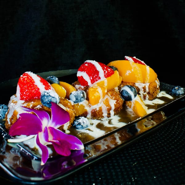 Three golden-brown French toast pieces topped with strawberries, blueberries, peaches, and cream drizzle.